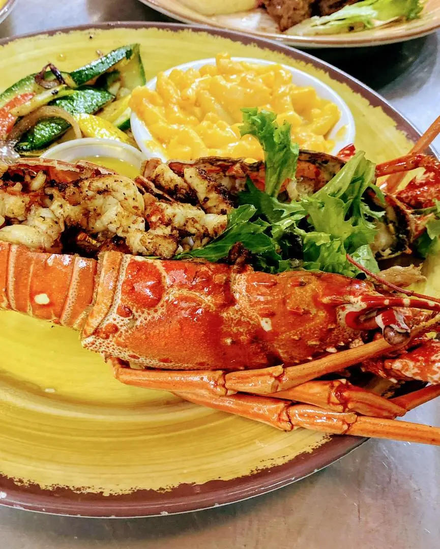 image shows a plate of food featuring a cooked lobster as the main element, accompanied by sides of mac and cheese and grilled vegetables